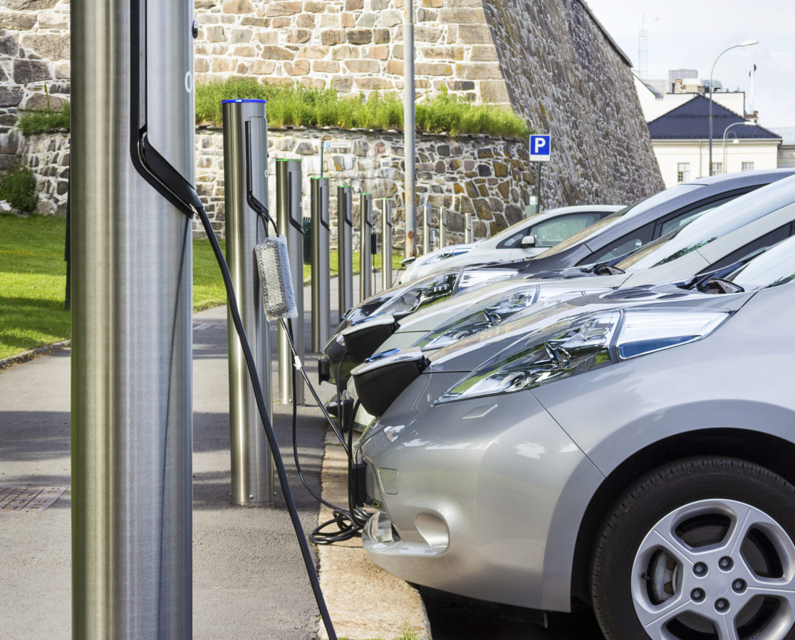 Elektroautos, die an modernen Ladesäulen vor einem Mehrfamilienhaus und einem Gewerbegebäude geladen werden – Symbol für zukunftssichere Immobilien